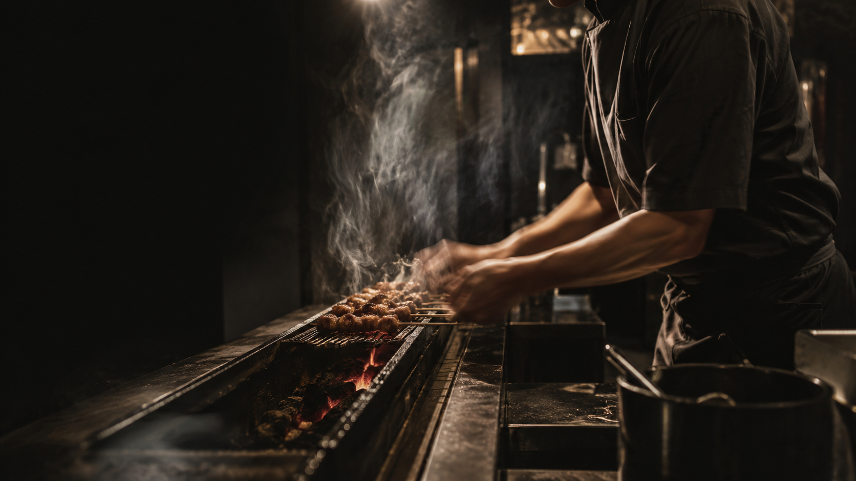 A chef working over open flame in the dark, contemporary Ember House kitchen — smoke rising, warm highlights catching the grill.