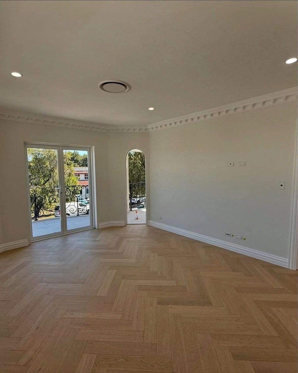 Herringbone oak flooring running the length of an empty room towards French doors