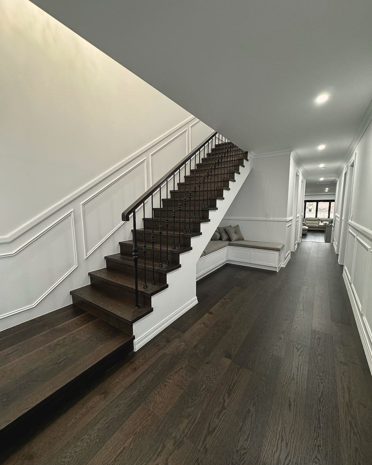 Hallway in dark plank flooring beside a staircase with a black balustrade and panelled walls