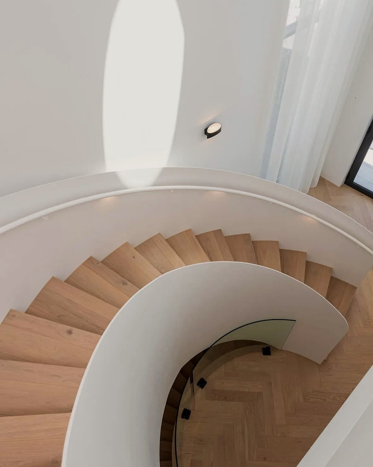 Curved staircase photographed from above, timber treads winding against a white wall
