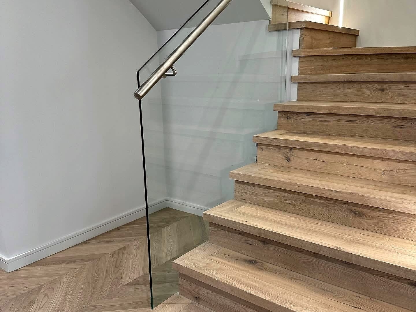Timber stair treads behind a glass balustrade, herringbone flooring at the base