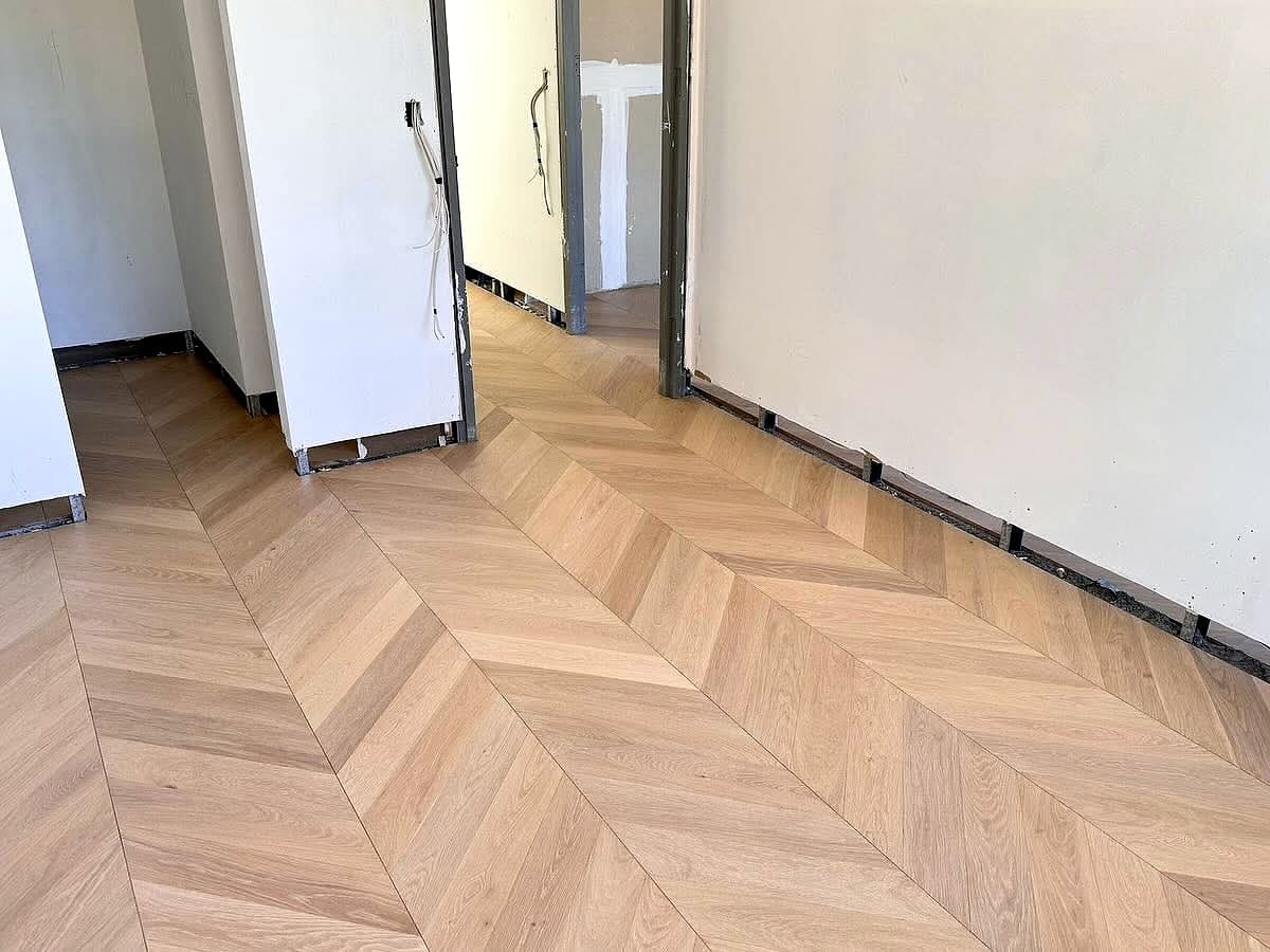 Chevron flooring running the length of a corridor towards an open doorway