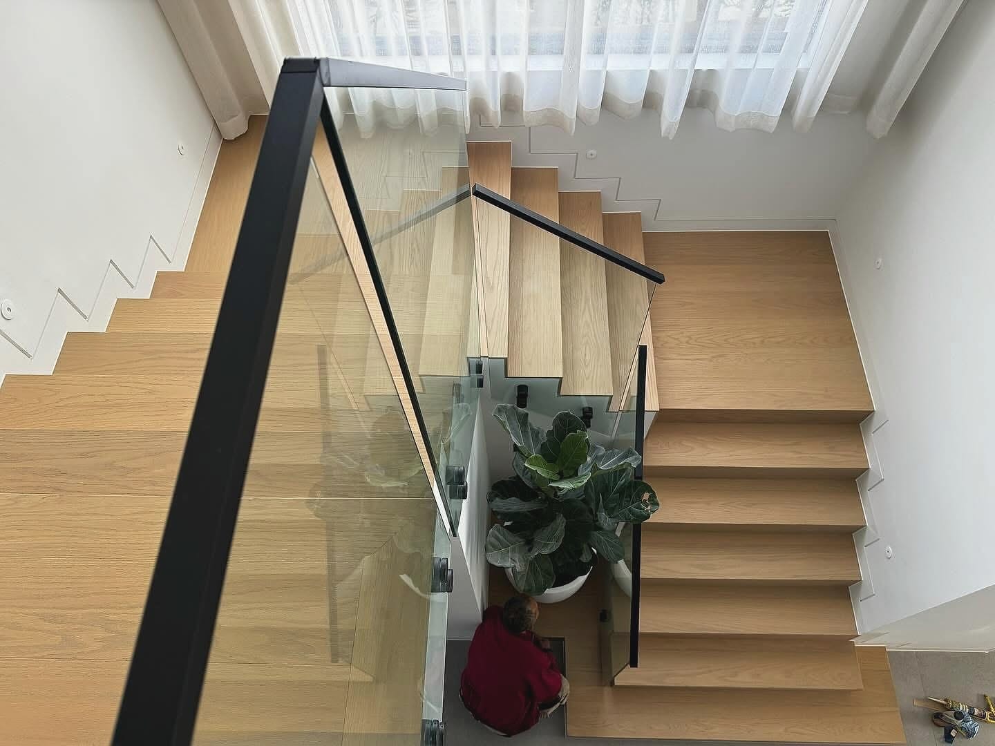 Staircase seen from above with glass and black metal balustrades, timber treads throughout