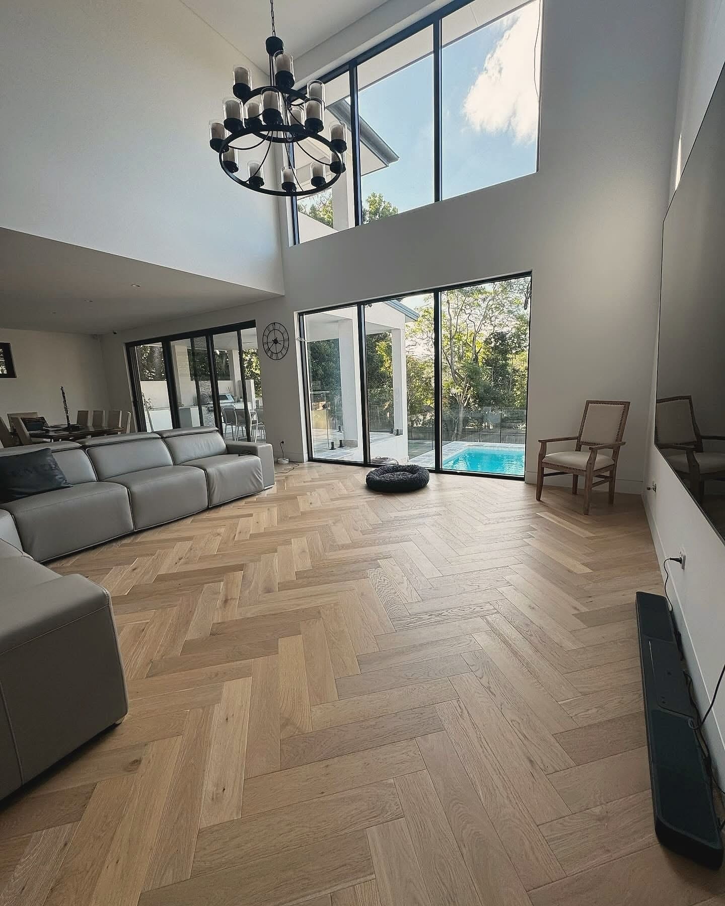 Double-height living space with herringbone flooring and sliding glass doors to a pool