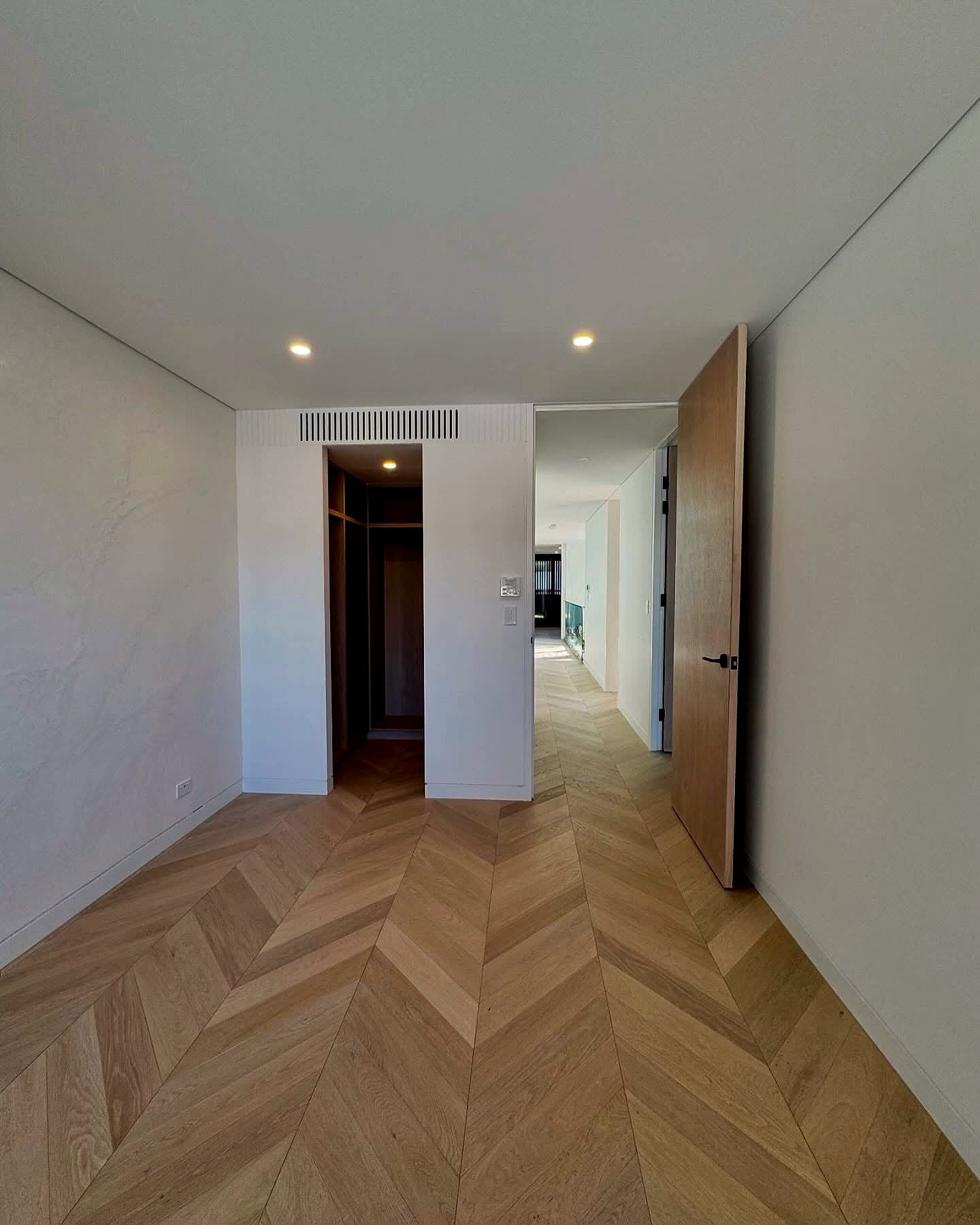 Chevron flooring running down a hallway past an open door