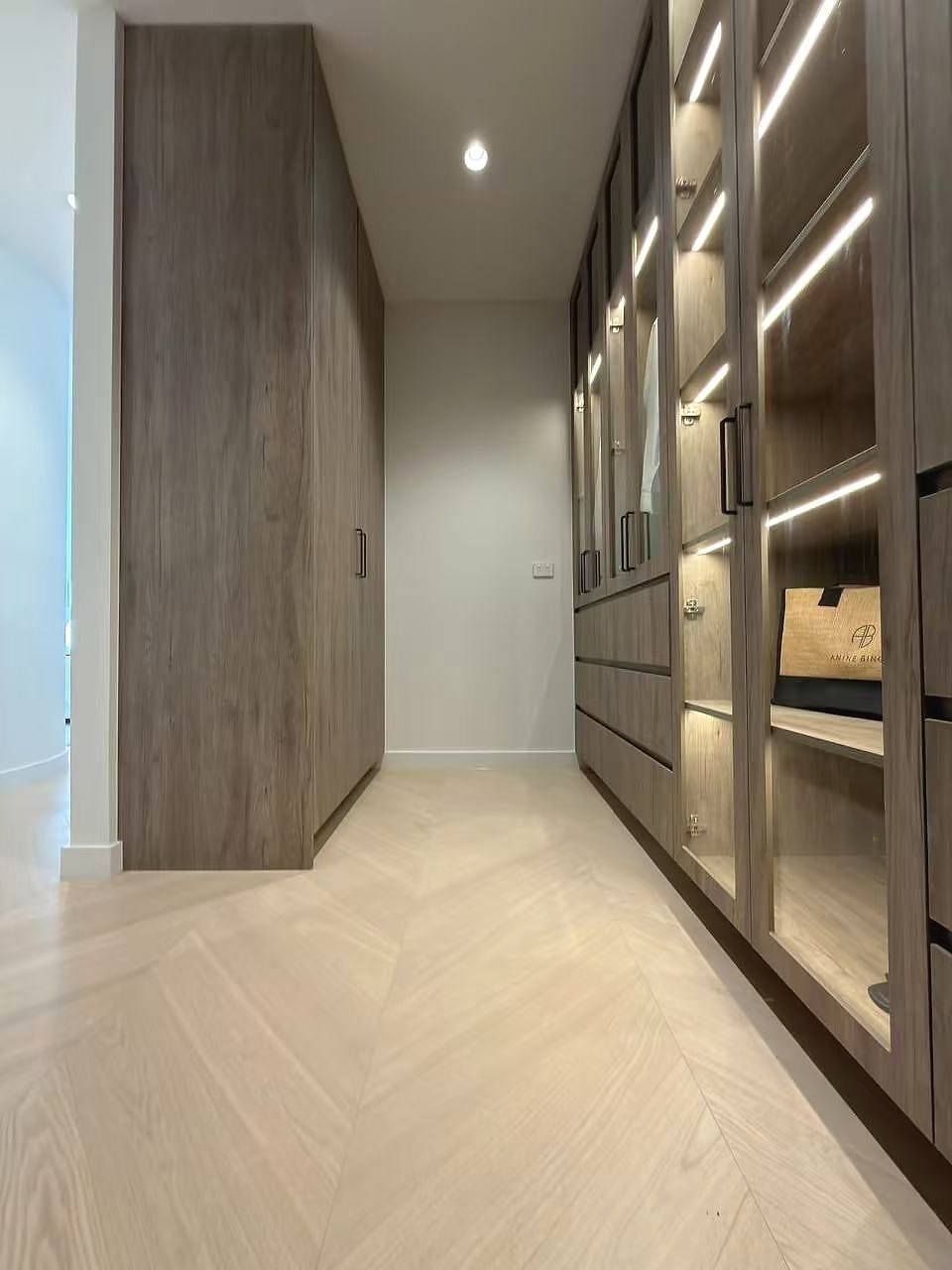 Dressing room with lit glass-fronted joinery above a herringbone floor