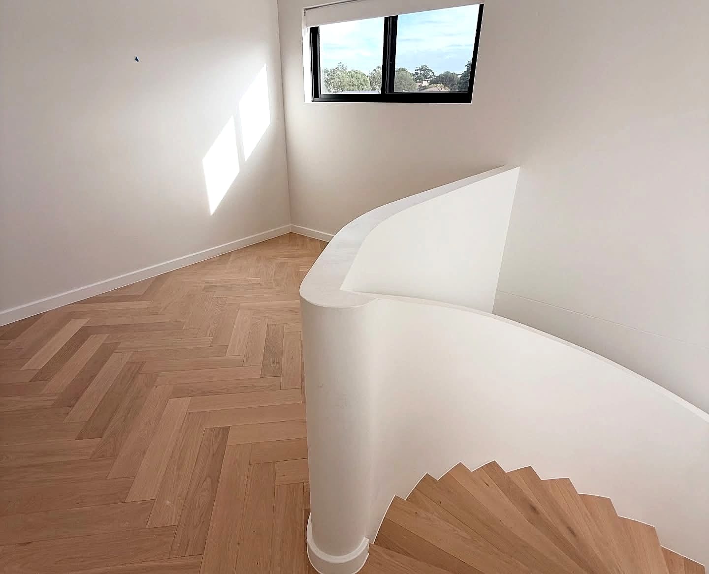 Curved staircase meeting a herringbone floor beside a corner window