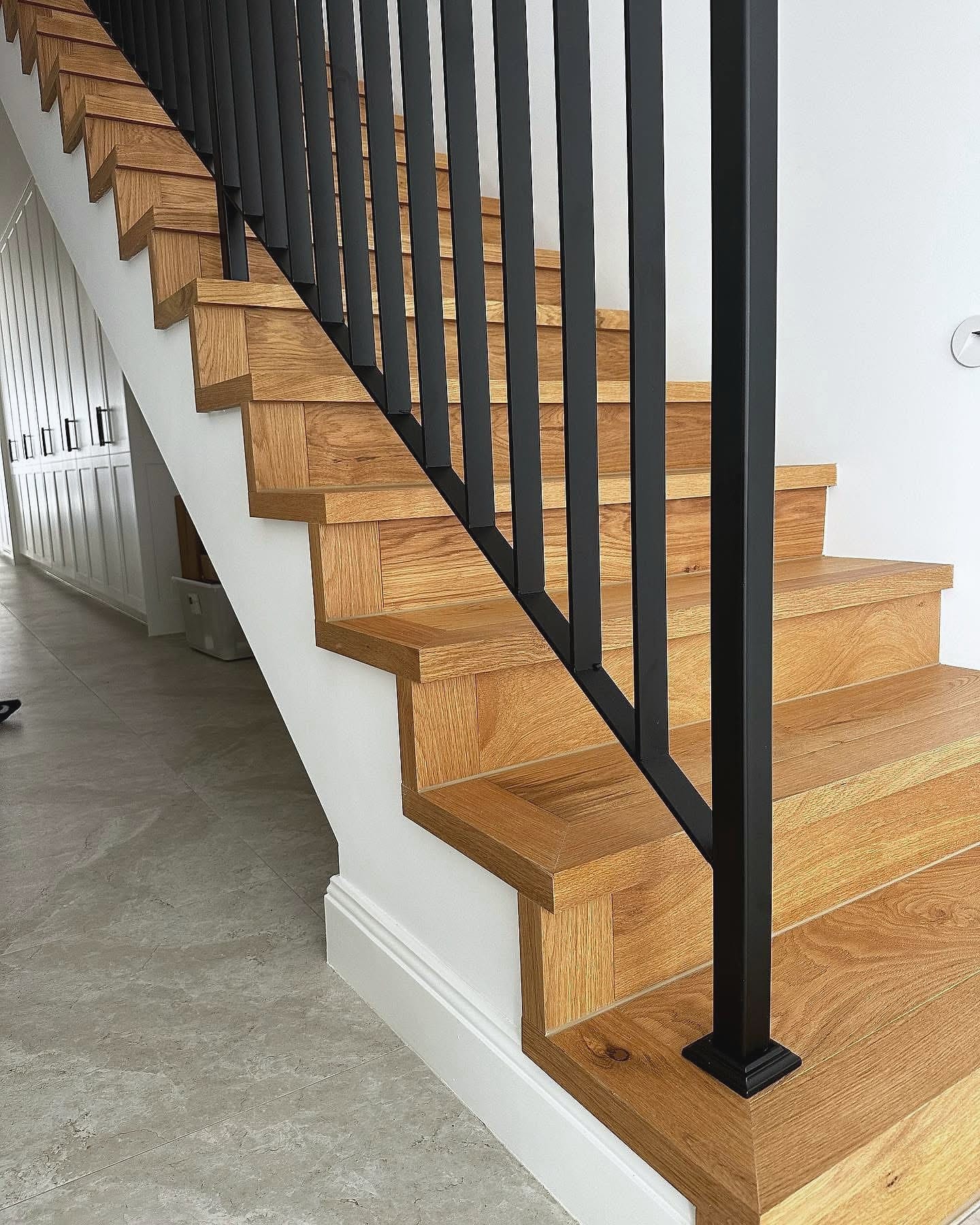 Timber staircase with a black metal balustrade rising from a tiled entry
