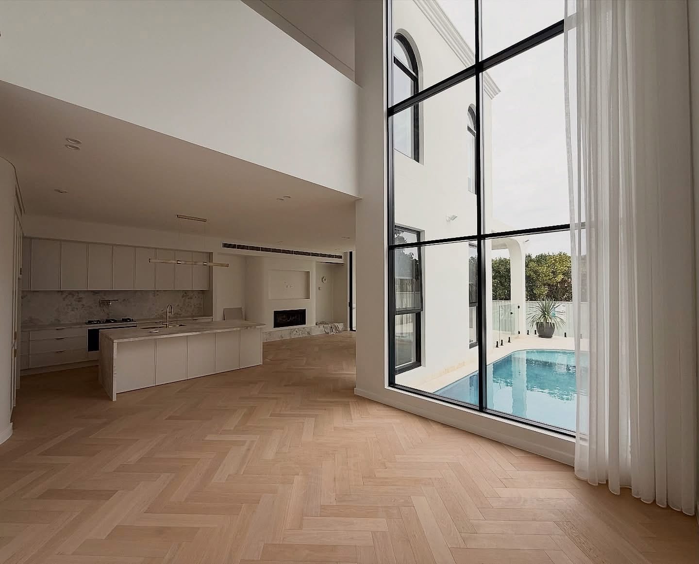 Open-plan living and kitchen under a double-height void, herringbone flooring throughout